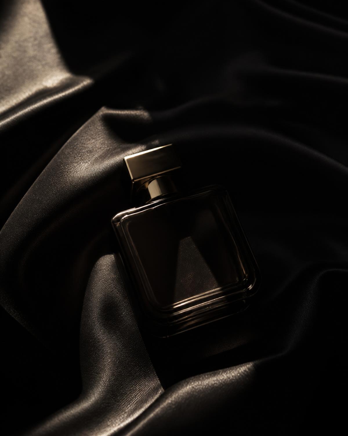 Frasco de perfume escuro repousando sobre seda preta