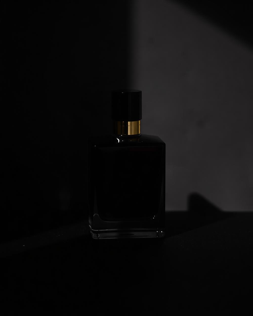 Frasco de perfume escuro iluminado por um feixe de luz sobre fundo preto